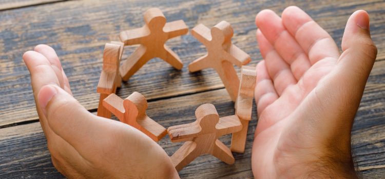 Business success concept on wooden background high angle view. hands protecting wooden figures of people.